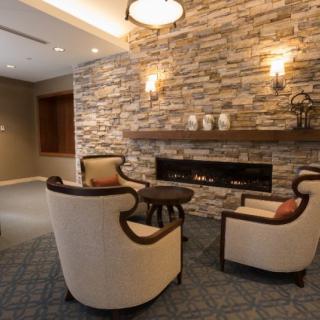 A cozy living room with a stone fireplace, surrounded by comfortable armchairs and soft lighting.