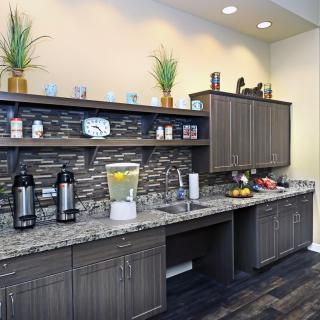 A modern kitchen area with granite countertops, cabinets, and a beverage station.