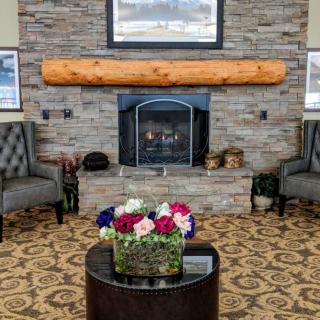A cozy living room with a stone fireplace, decorated with armchairs and a coffee table featuring a colorful flower arrangement.