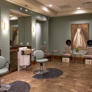 A cozy and neatly arranged salon interior with chairs, mirrors, hairdryers, and artwork on the wall.