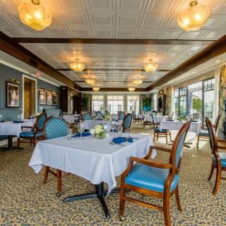 An elegant dining room setup with neatly arranged tables and chairs, decorated with chandeliers and carpeting, offering a sophisticated atmosphere.