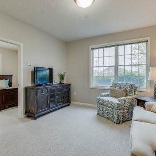 A cozy living room with a TV, comfortable seating, and ample natural light from a large window.