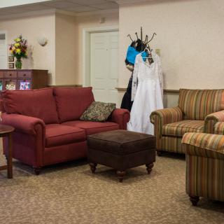 A cozy living room with various furniture pieces, including a red sofa and a coat rack with a white dress.