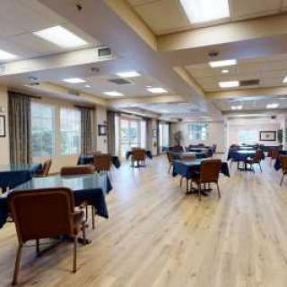 A spacious and well-lit dining area with several tables and chairs arranged on a wooden floor.
