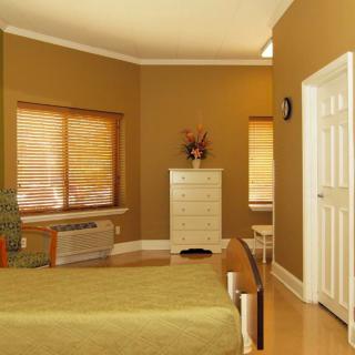 A cozy bedroom with warm-toned walls, featuring a bed, chest of drawers, and window blinds.