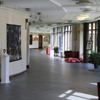A well-lit indoor hallway featuring art displays, plants, and comfortable seating.