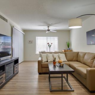 A modern living room featuring a comfortable L-shaped sofa, a flat-screen TV, and a stylish coffee table beneath a ceiling fan and large window.