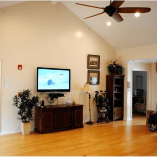 A cozy living room with a wall-mounted television, wooden flooring, and a ceiling fan.