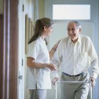 A healthcare worker assists an elderly man using a walker.