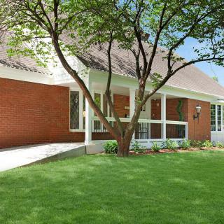 A brick house with a well-maintained lawn and a large tree in the front yard.
