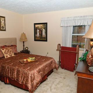 A cozy bedroom with a neatly made bed, decorated in warm tones, featuring lamps and artwork on the walls.