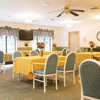 A bright and inviting dining area, furnished with tables covered in yellow tablecloths and comfortable seating, ideal for community gatherings.