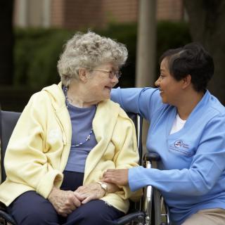 A caregiver and an elderly woman share a warm moment outdoors.
