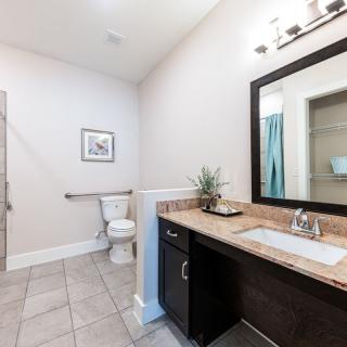 A modern, spacious bathroom with a large mirror and sink area, featuring a tiled floor and a toilet in the corner.