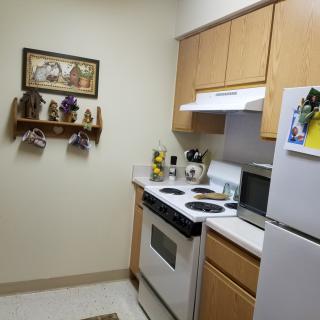A cozy kitchen with traditional wooden cabinets, a stove, refrigerator, microwave, and decorative wall art.