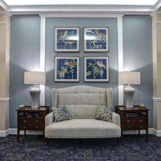 A cozy living room setting with a central sofa, flanked by side tables and lamps, beneath framed artwork.