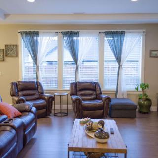 A cozy living room with leather sofas, a coffee table, and large windows with curtains.