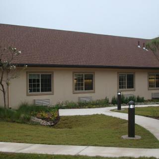 A single-story building surrounded by a landscaped area and a curved pathway.