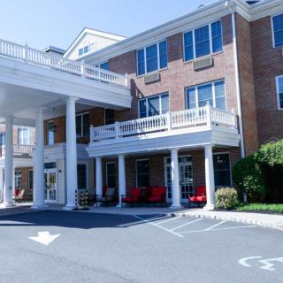 A large building with a columned entrance and multiple windows, featuring a parking area in front.