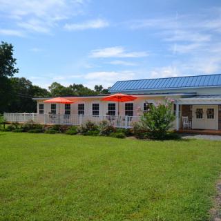 A small building with a blue roof and outdoor patio umbrellas, surrounded by green grass under a clear blue sky.