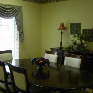 A dining room with a wooden table and chairs, decorated with a lamp and floral arrangement.