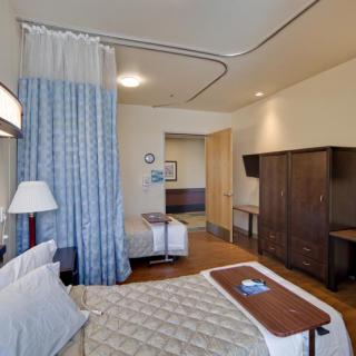 A hospital room with a patient bed, curtain, and TV.