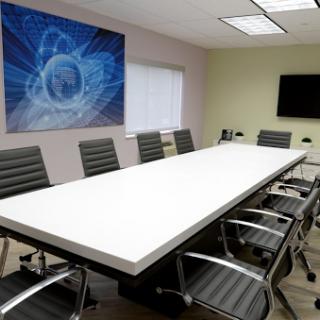 A modern conference room featuring a long white meeting table surrounded by ergonomic chairs and a blue abstract artwork.