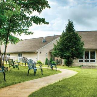 A peaceful outdoor area with a pathway leading to a building, surrounded by trees and grass.