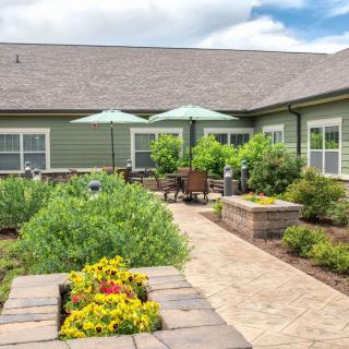 A beautifully landscaped courtyard featuring a garden with vibrant flowers, a paved walkway, and outdoor seating with umbrellas.