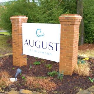 Entrance sign for a place named 'August' with decorative landscaping.