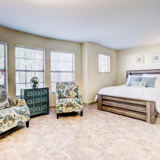 A cozy bedroom with a large bed, floral armchairs, and ample natural light.