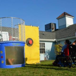 A person in a wheelchair aiming to hit the target of a dunk tank outdoors on a sunny day.