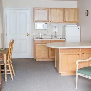 A small kitchen area with wooden cabinets, a refrigerator, and a dining table with chairs.