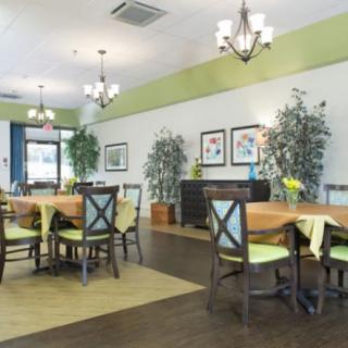 A well-decorated dining room with tables and chairs, illuminated by chandeliers and adorned with plants and wall art.