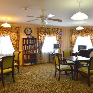 A cozy library reading area with tables, chairs, and a bookshelf under warm lighting.