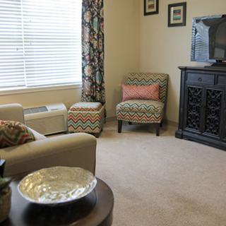 A cozy living room with patterned armchairs, an ottoman, and a decorative cabinet.