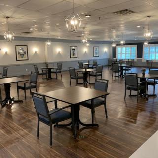 An empty dining room with neatly arranged tables and chairs, featuring a modern decor and wooden flooring.