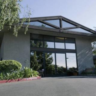 A modern building with a large glass entrance and surrounding greenery.
