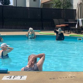A group of people participating in a water aerobics class in an outdoor swimming pool.
