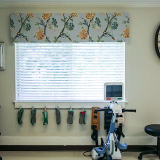 A well-lit interior space featuring a window adorned with floral valance and exercise equipment arranged nearby.