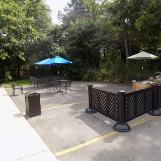 A quiet outdoor patio area with tables, chairs, and umbrellas surrounded by trees.