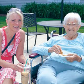 A joyful moment shared between a younger and an elderly woman enjoying food and drinks outdoors.