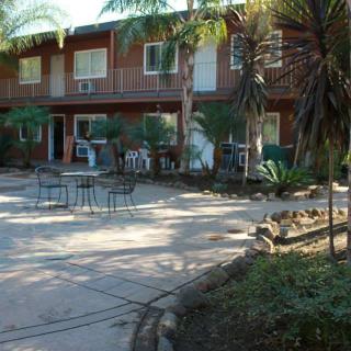 A two-story house with a garden and outdoor seating area surrounded by palm trees.