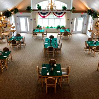 A spacious banquet hall with tables covered in green tablecloths, decorated with chandeliers and festive banners.