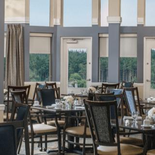A well-lit dining area with elegant tables and chairs, offering a view through large windows.