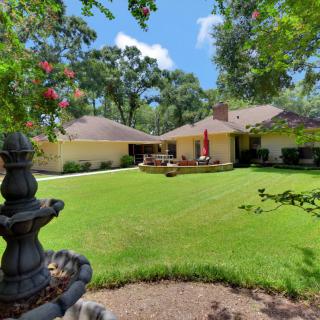 A spacious backyard with a well-maintained lawn and garden, featuring a patio area surrounded by trees.