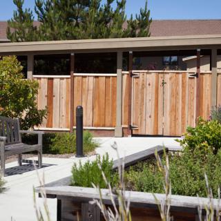 A serene outdoor space featuring a wooden fence, greenery, and a bench along a paved pathway.