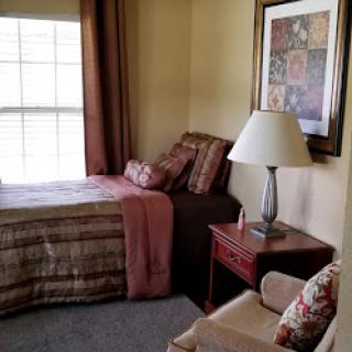 A cozy and well-decorated corner of a bedroom featuring a bed with decorative pillows, a lamp on a nightstand, and artwork on the wall.