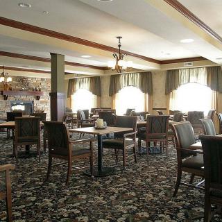 An empty dining area with tables and chairs arranged neatly, featuring large windows and a patterned carpet.