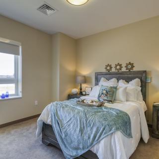 A cozy bedroom with a neatly made bed, featuring blue blankets and decorative pillows, flanked by nightstands and lamps.